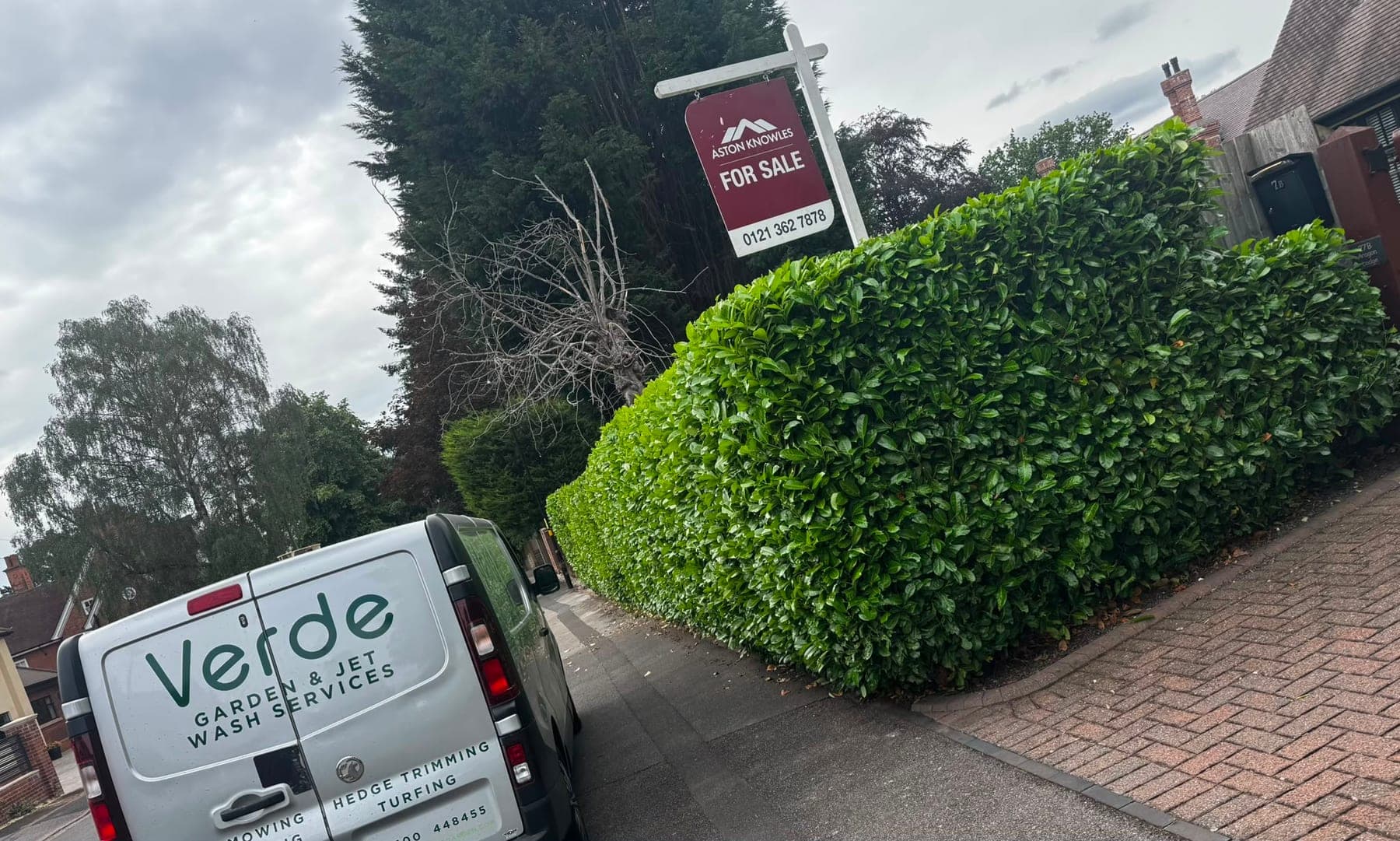 A clipped laurel hedge outside a property for sale, with the Verde van alongside