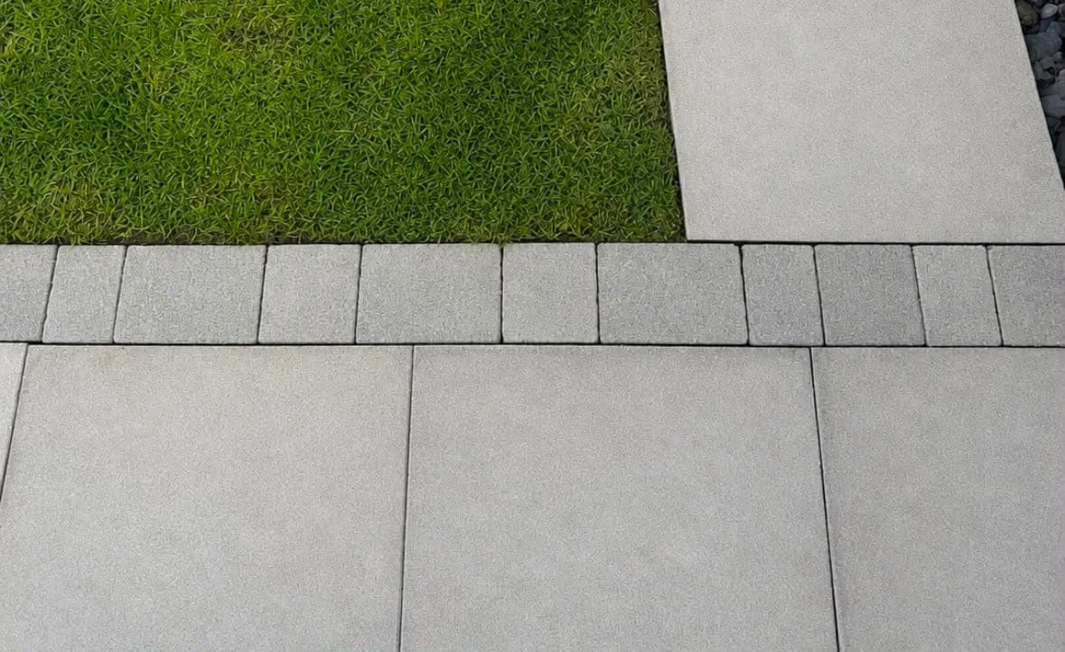 Freshly washed grey paving slabs meeting a clean lawn edge and setts